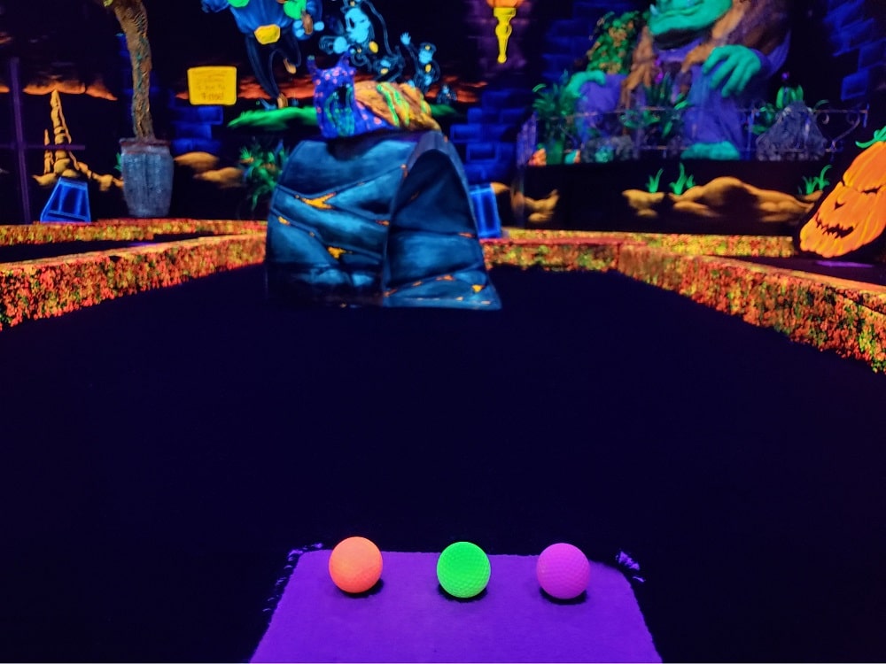 A neon orange, green and purple golf ball on a glow-in-the-dark indoor mini golf course at monster mini golf.